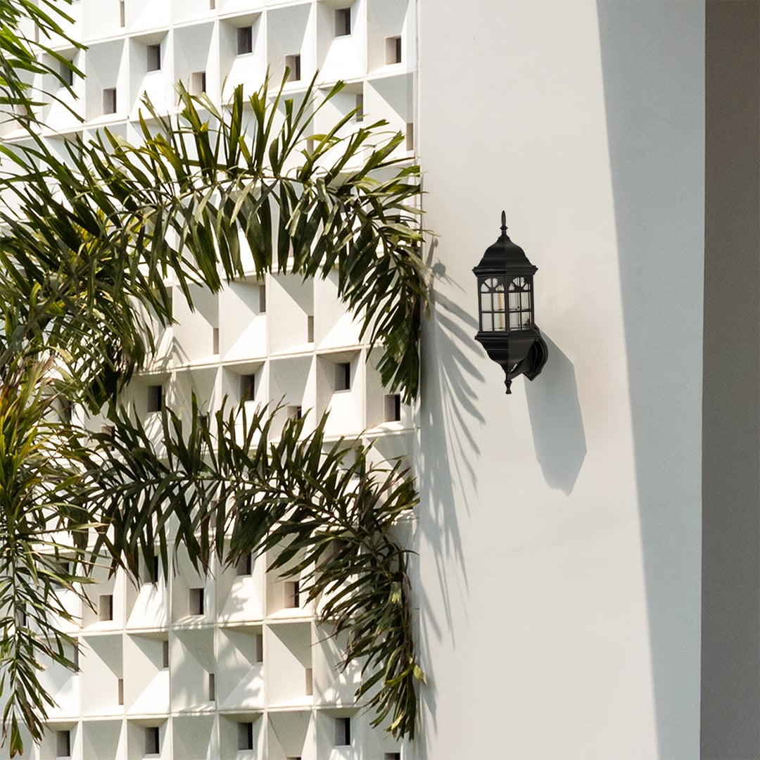 Black metal outdoor wall light lifestyle image with arched windowpane frame mounted on white villa wall by palm trees.