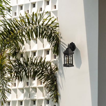 Black outdoor lantern with the light off installed on a bright exterior wall highlighting its traditional hexagon frame and arched window style glass design.