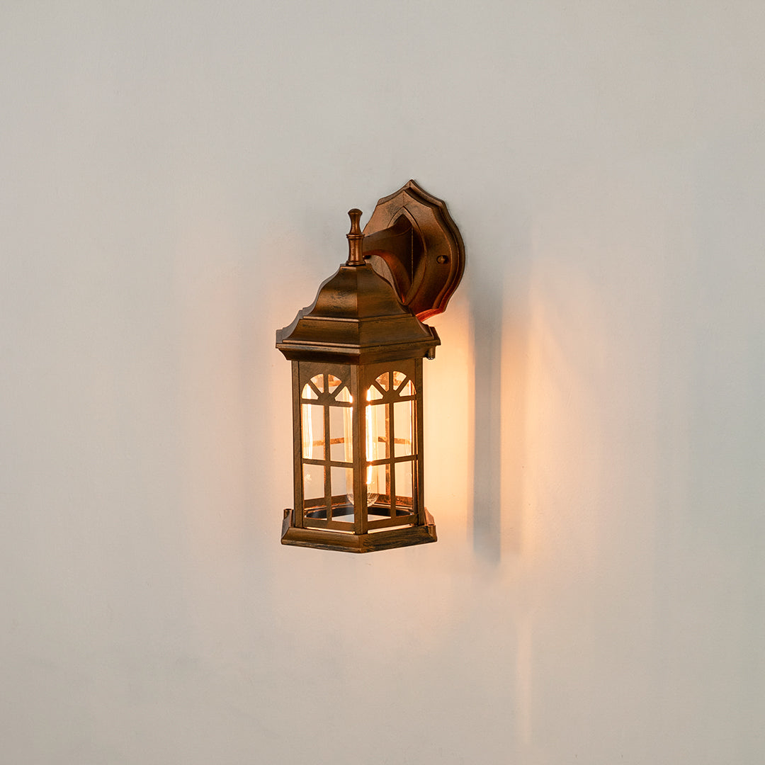 Antique brass outdoor wall lantern on white background with an arched paneled glass shade for vintage porch decor.