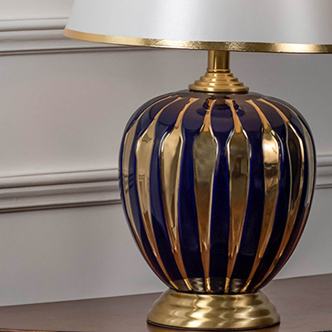 Closeup of blue ceramic table lamp with bold gold stripes brass base and fabric shade for luxury home decor.