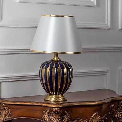 Blue ceramic table lamp turned off with golden striped base and fabric lampshade displayed on plain white background.