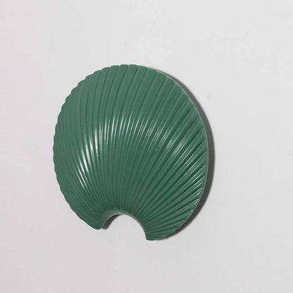 A contemporary shell pattern wall decor piece in deep green presented against a bright white backdrop offering a clear view of its curved textured detailing.