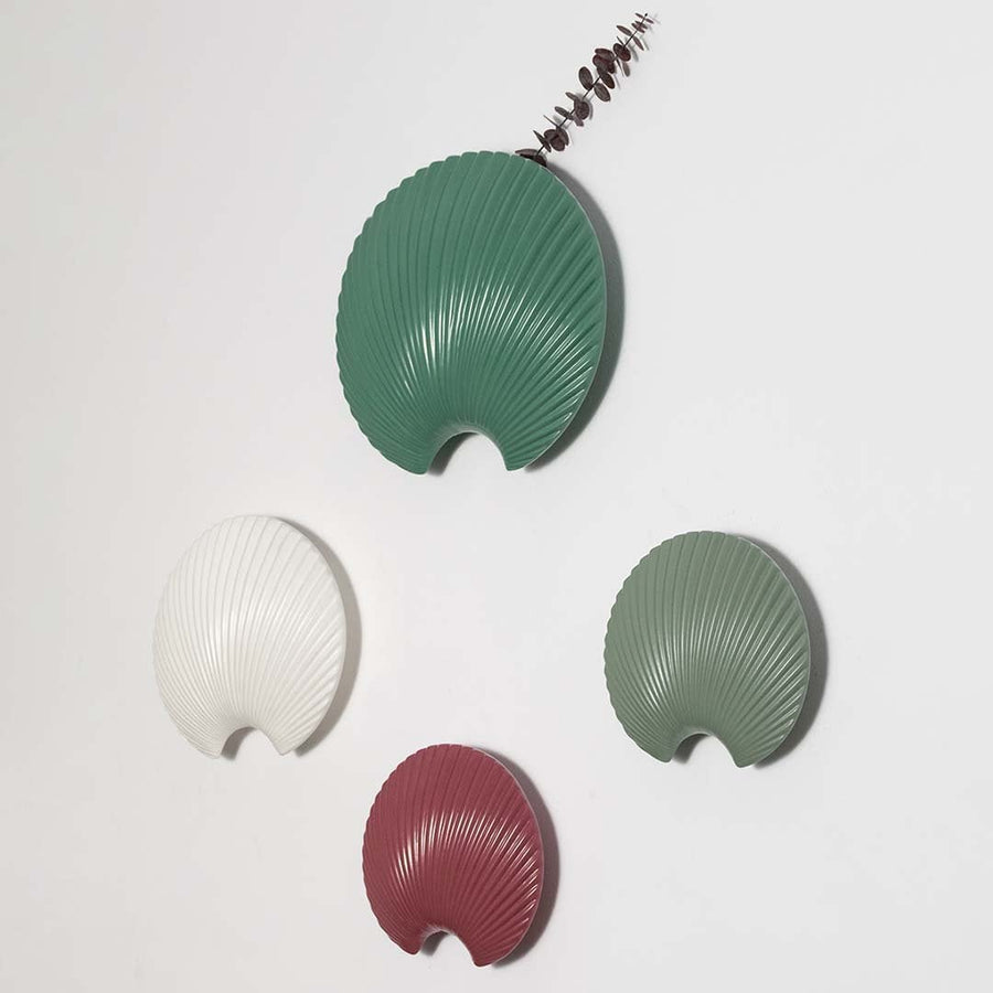 A white shell inspired wall decor piece shown as part of a styled grouping highlighting its curved sculpted form and refined texture for contemporary interiors.