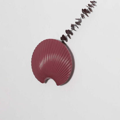 A sculpted maroon shell wall decor piece photographed on a plain white surface showcasing its smooth contours and detailed ridges for a refined aesthetic.