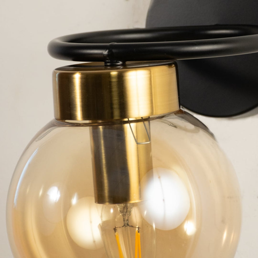 Closeup of black and gold wall light showing amber glass globe and sleek circular metal frame ideal for modern decorative interior lighting.