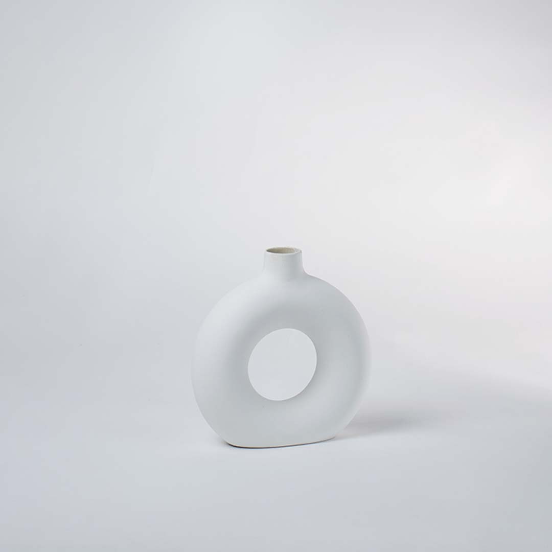 Minimalist round white ceramic vase with hollow center on a plain background – modern home decor vase.