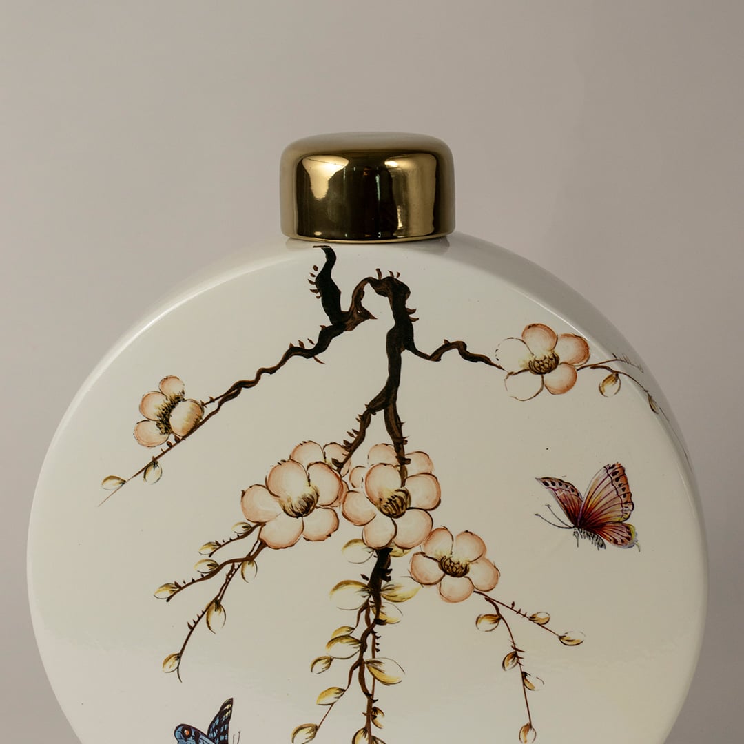 Closeup of round ceramic jar showing gold lid and intricate branch and butterfly artwork.