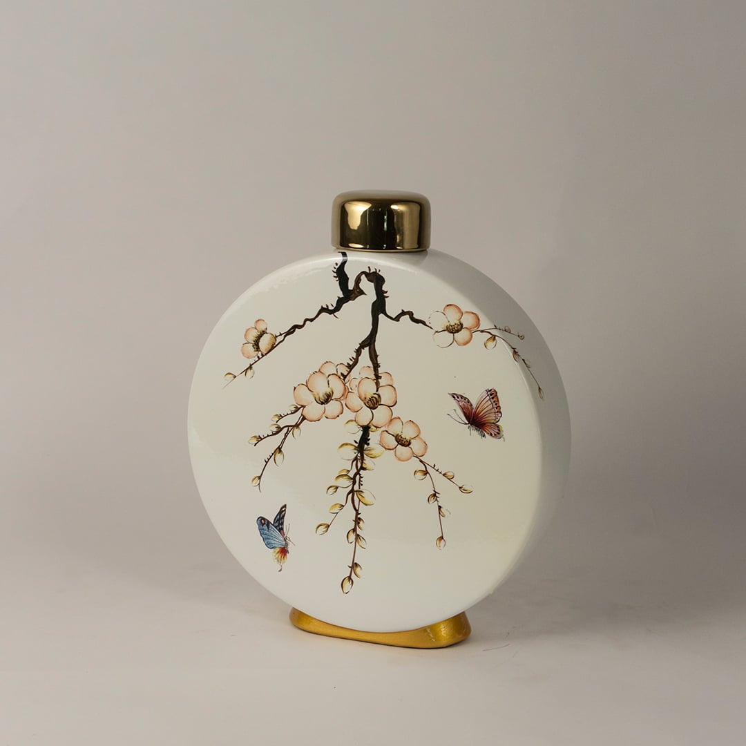 Side angle view of round ceramic jar showing elegant floral branches and butterfly painting with gold detailing.