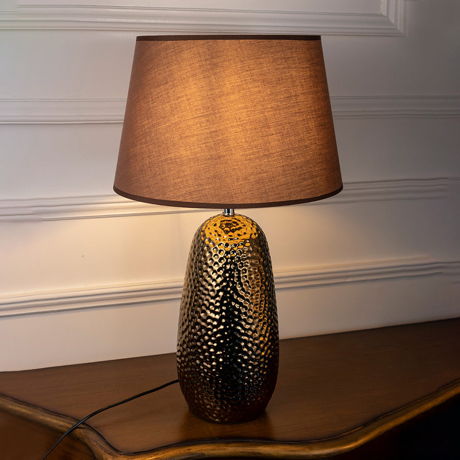 Black textured ceramic table lamp with warm glowing shade and gold accent creating cozy ambient lighting for side tables.