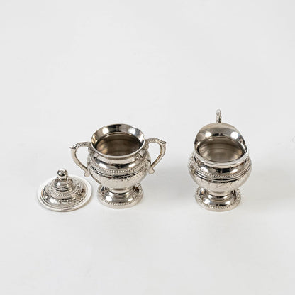 Silver sugar bowl and creamer with lid removed showing interior and detailed engraving on white background.