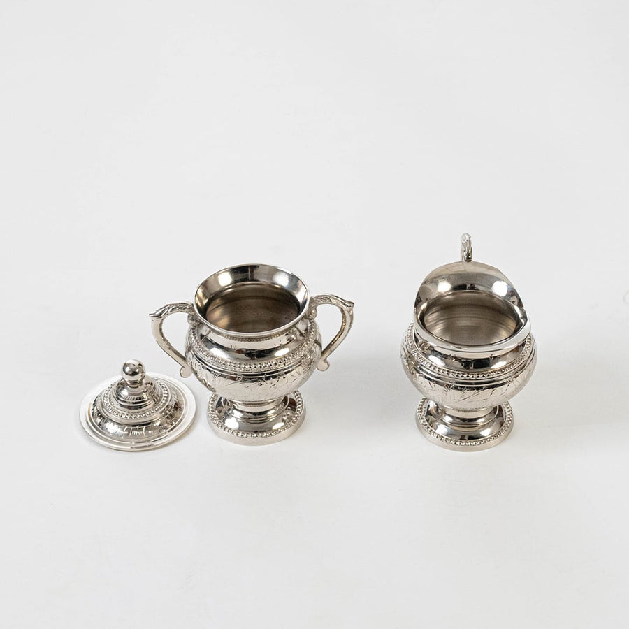 Silver sugar bowl and creamer with lid removed showing interior and detailed engraving on white background.