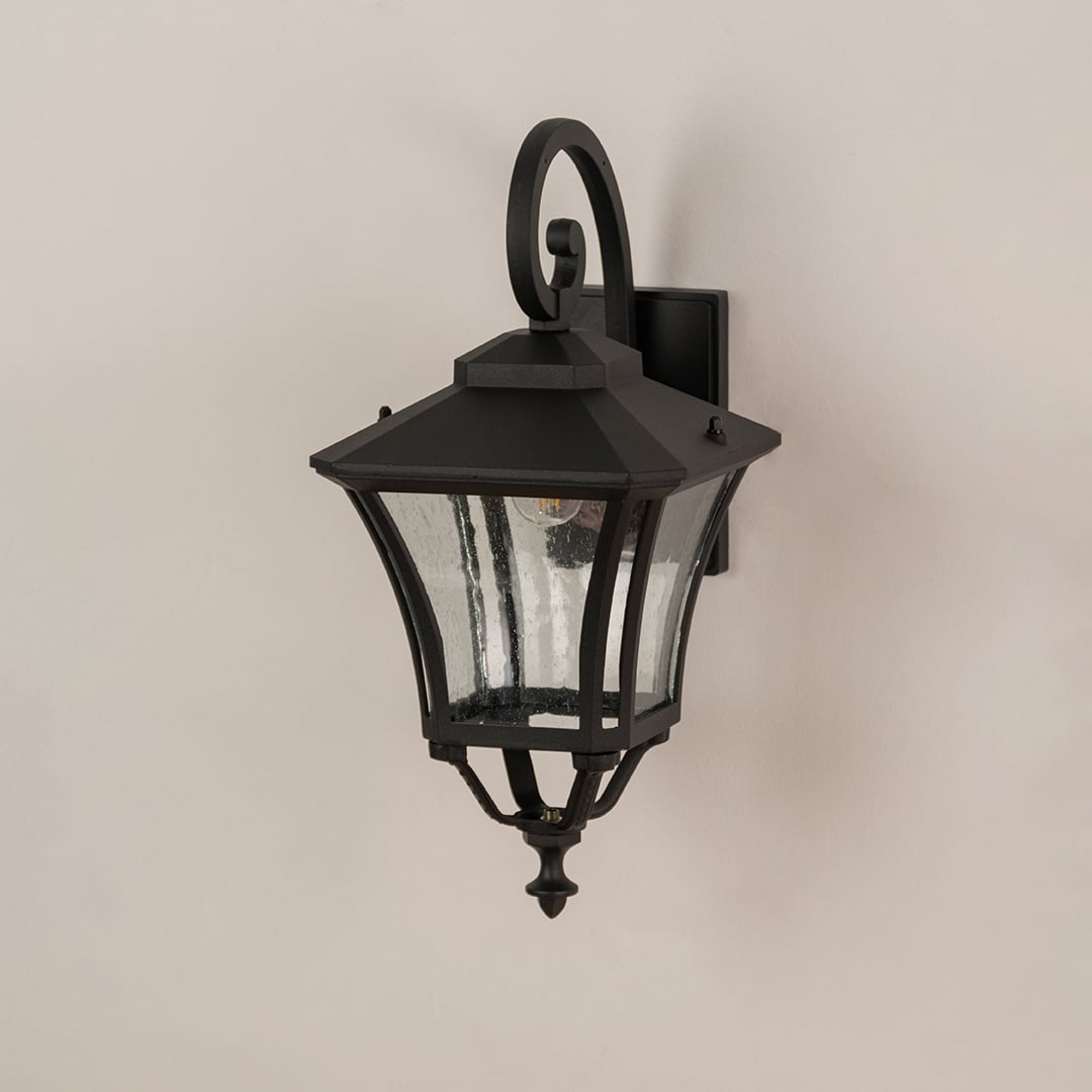 Black metal outdoor wall lantern with clear textured glass shown off to highlight design for exterior home settings.
