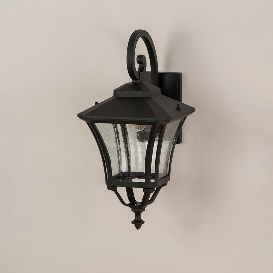 Black metal outdoor wall lantern with clear textured glass shown off to highlight design for exterior home settings.