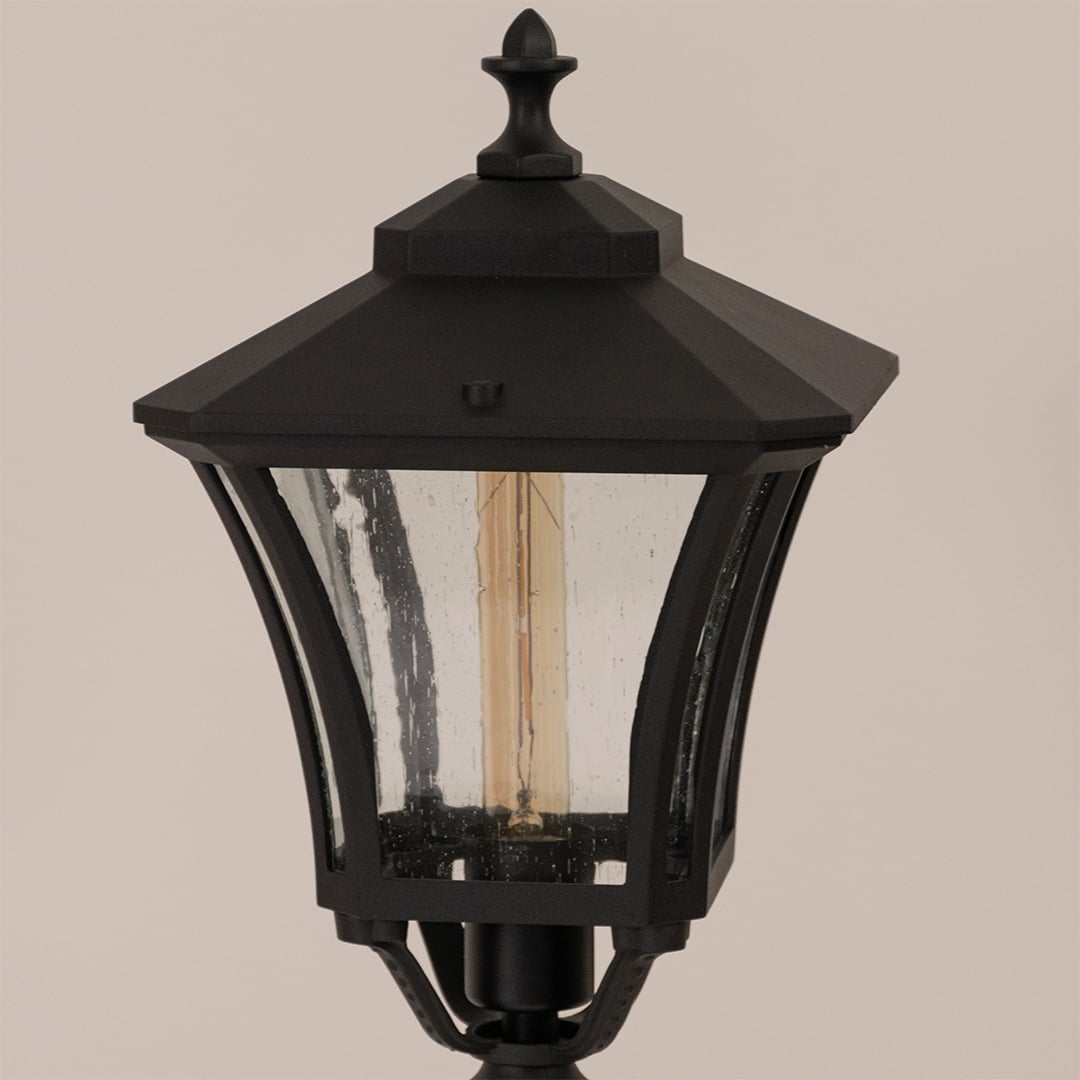 Close up view of black lantern head with clear glass panels and ornate decorative finial top detail craftsmanship.