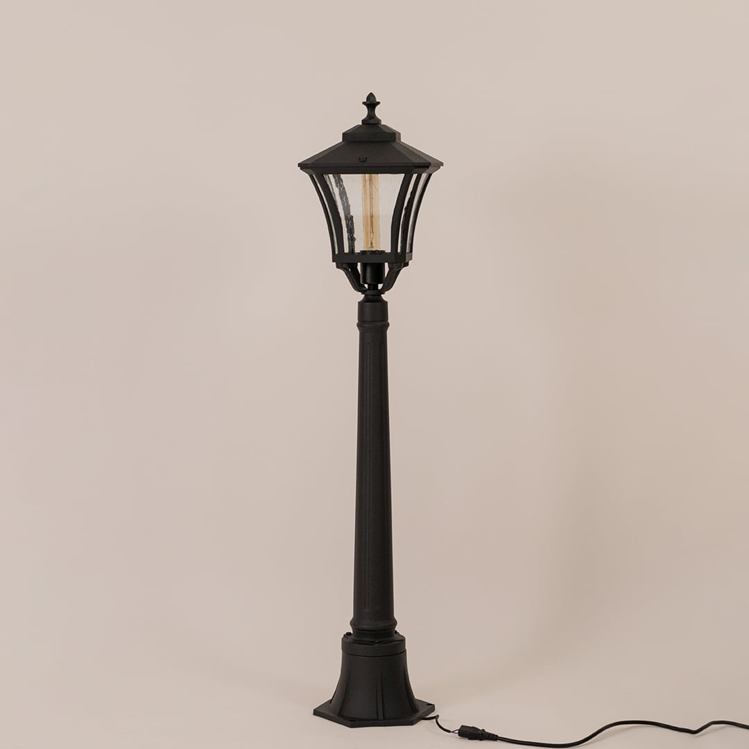 Classic black metal outdoor post light fixture with clear glass lantern switched off on minimal white backdrop.