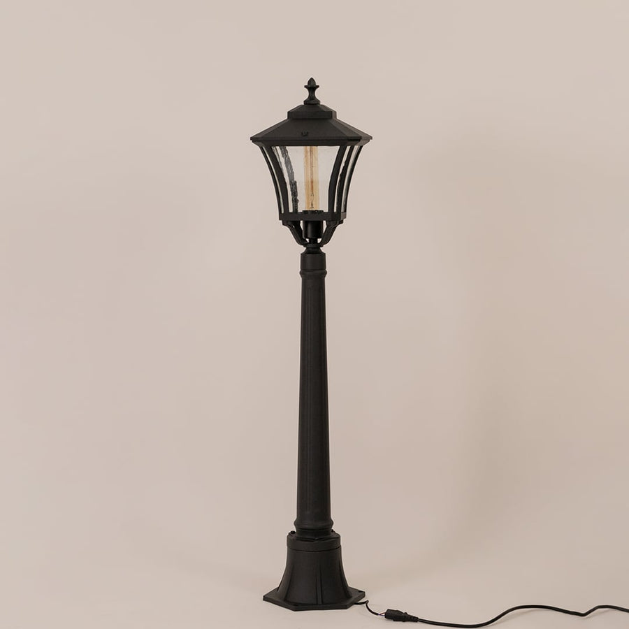 Classic black metal outdoor post light fixture with clear glass lantern switched off on minimal white backdrop.