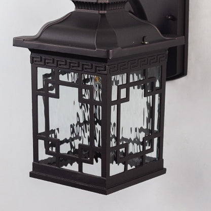 Closeup of black outdoor wall light with intricate glass and warm bulb glow.