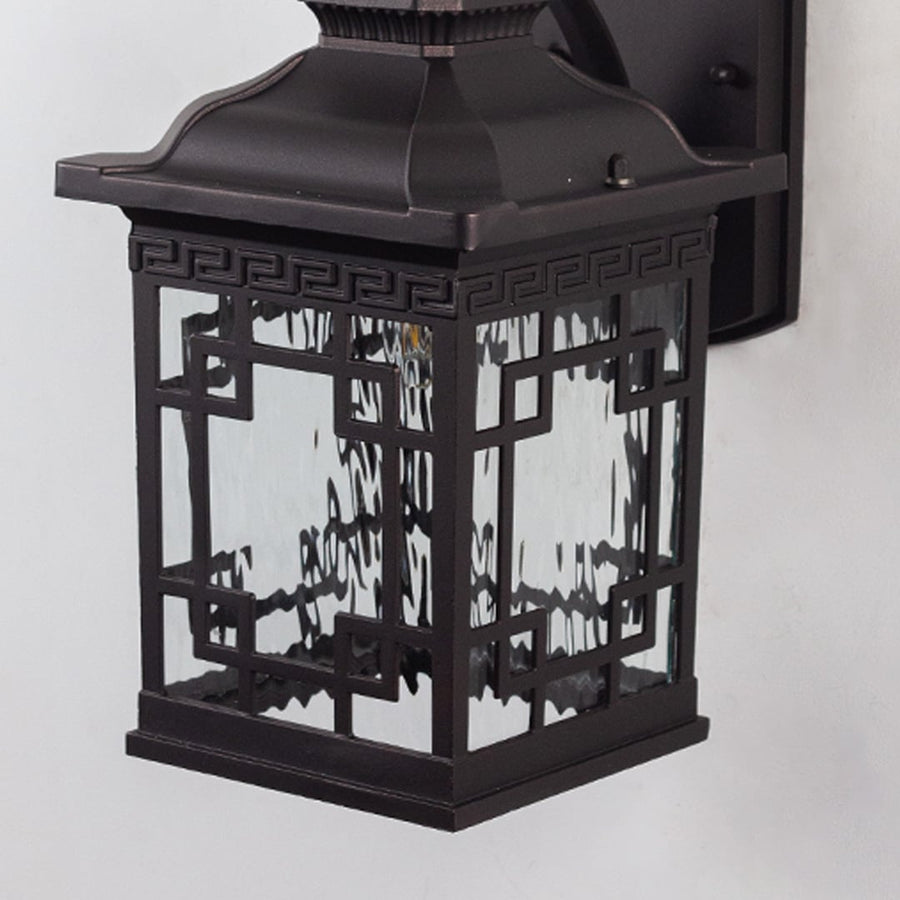 Closeup of black outdoor wall light with intricate glass and warm bulb glow.