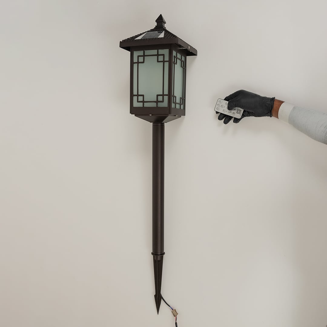 Brown solar powered garden spike lantern with frosted patterned glass shown with light off on a white background displaying its tall spike frame and classic style.