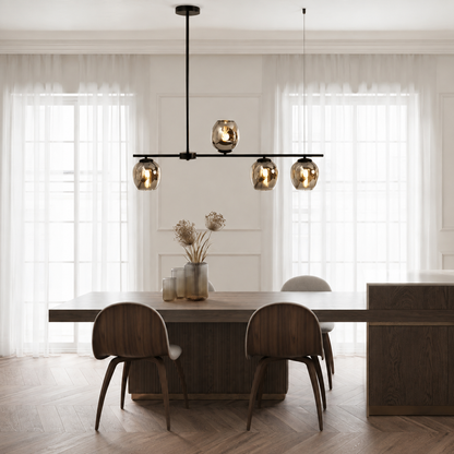 Modern linear pendant chandelier with four reflective gold-toned glass shades hanging above a wooden dining table in a bright, contemporary dining room.