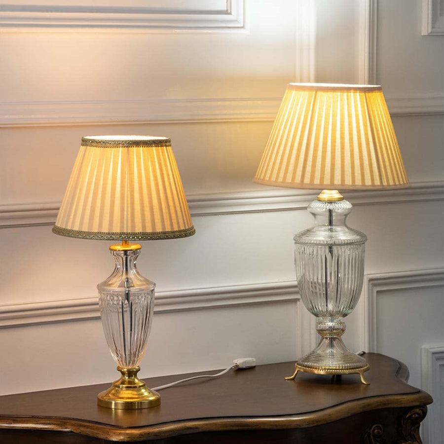 Pair of crystal glass table lamps with gold bases and pleated beige shades turned on together adding soft warm illumination to classic home interiors.