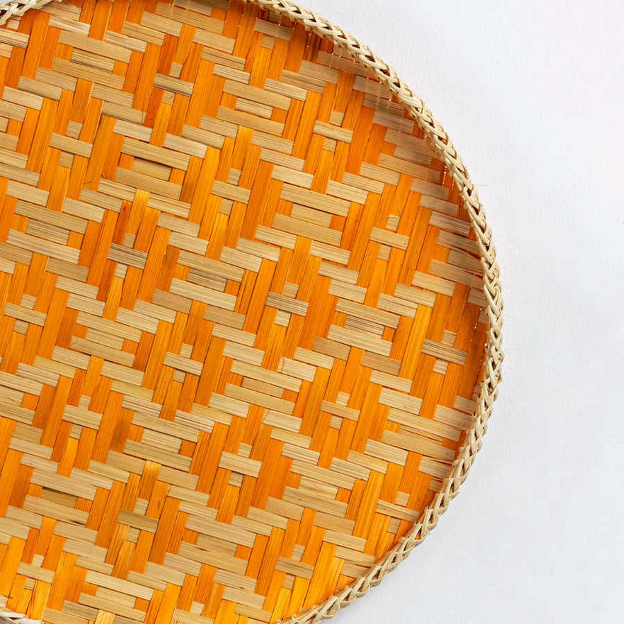 Closeup of handwoven wall basket edge showing bright orange geometric weave pattern highlighting natural fiber texture and artisan craftsmanship.