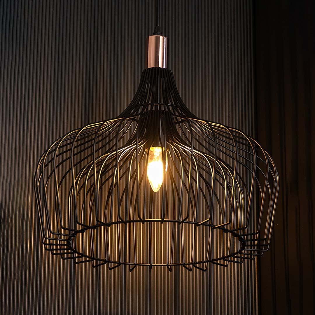 Black wire pendant lamp glowing softly against a dark background showcasing its open metal structure and warm illuminated center.