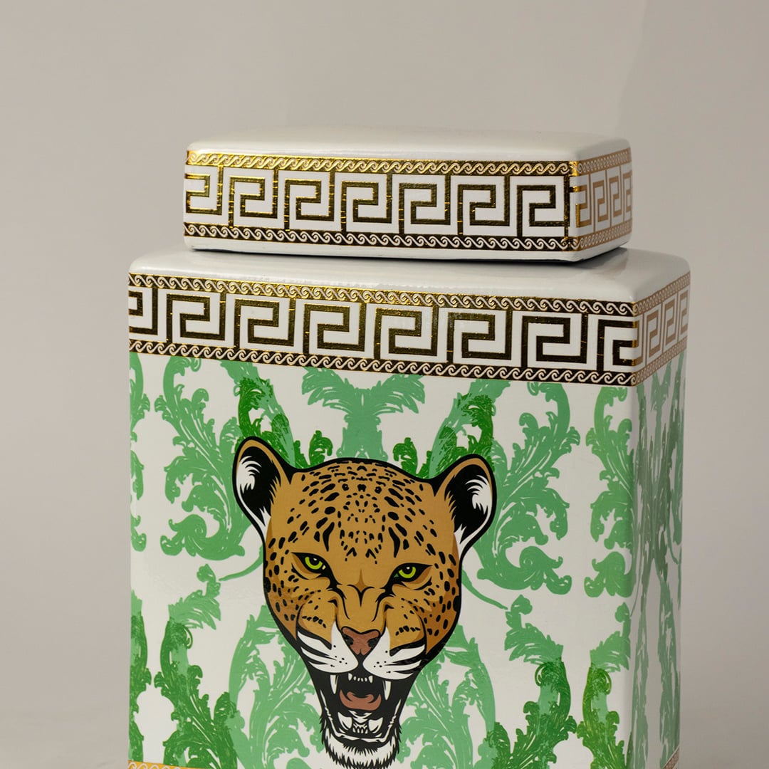 Closeup of white ceramic jar showing fine gold edging and detailed green foliage surrounding a leopard face.