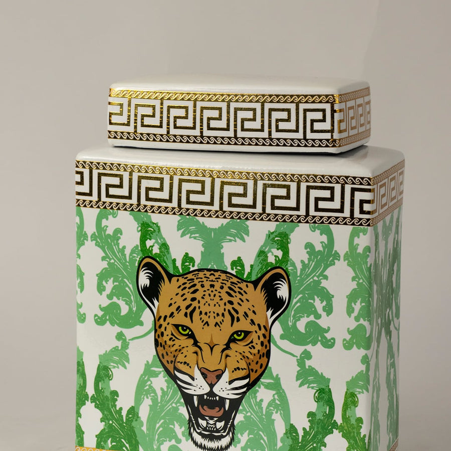 Closeup of white ceramic jar showing fine gold edging and detailed green foliage surrounding a leopard face.