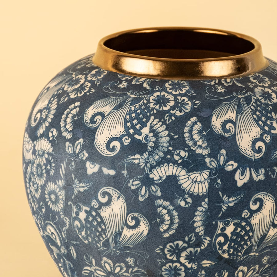 Closeup view of blue ceramic decor vase showing detailed floral pattern and smooth glazed texture with gold rim finish on warm neutral background.