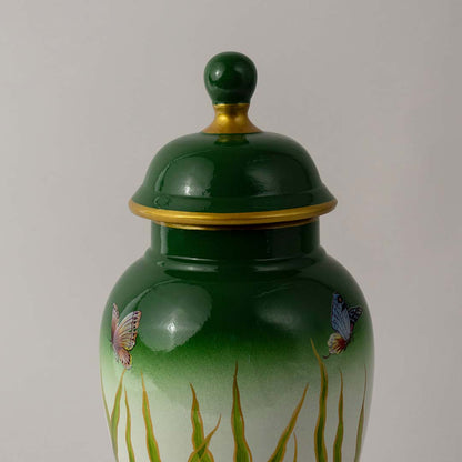 Closeup of ceramic decor jar showing detailed butterfly art with glossy green finish and golden accent detailing