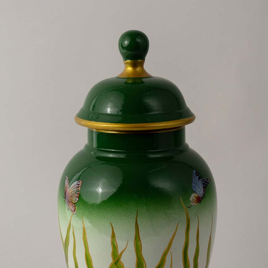 Closeup of ceramic decor jar showing detailed butterfly art with glossy green finish and golden accent detailing