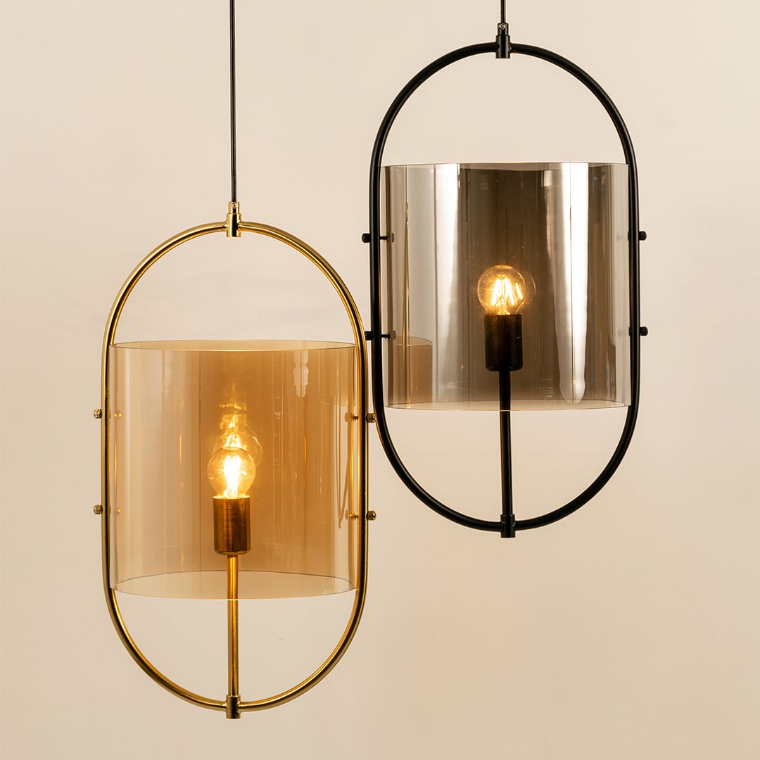 Close-up of a contemporary set of two pendant lights with oval frames in gold and black  featuring tinted glass shades softly glowing.