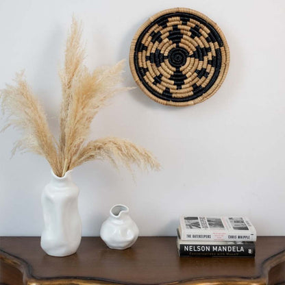 Black handwoven sea grass hanging wall basket with floral pattern styled above console enhancing boho interior walls with natural texture.