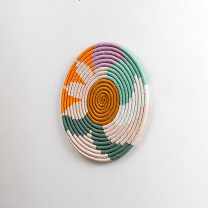 Round handwoven cotton wall plate with colorful green orange pink and cream pattern captured from a side angle on a dark background for bold modern styling.