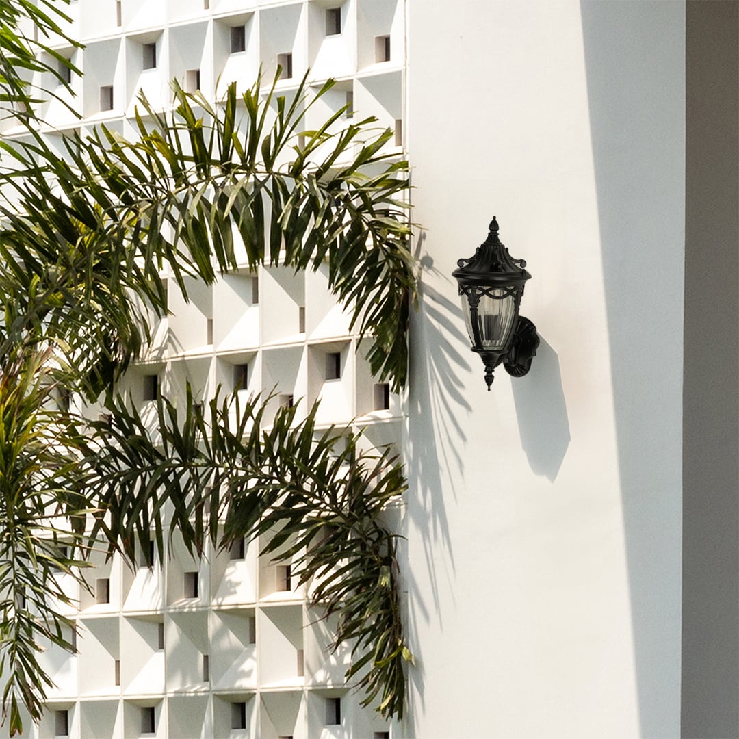 Black decorative outdoor lantern with the light off mounted on a bright exterior wall showcasing its vintage curved top frame and ribbed clear glass design.