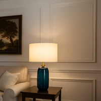 Blue ceramic lamp on side table with light on and beige wall background for calming bedroom décor.