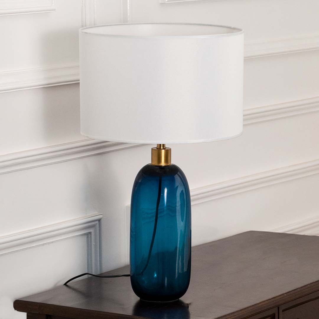 White shade blue glass lamp on wooden table with light on and white wall background for clean modern décor.