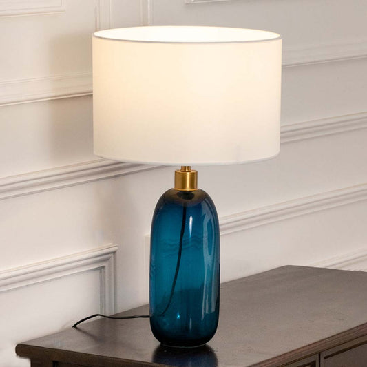 Blue glass table lamp with fabric shade placed on a wooden console table creating refined contemporary lighting.