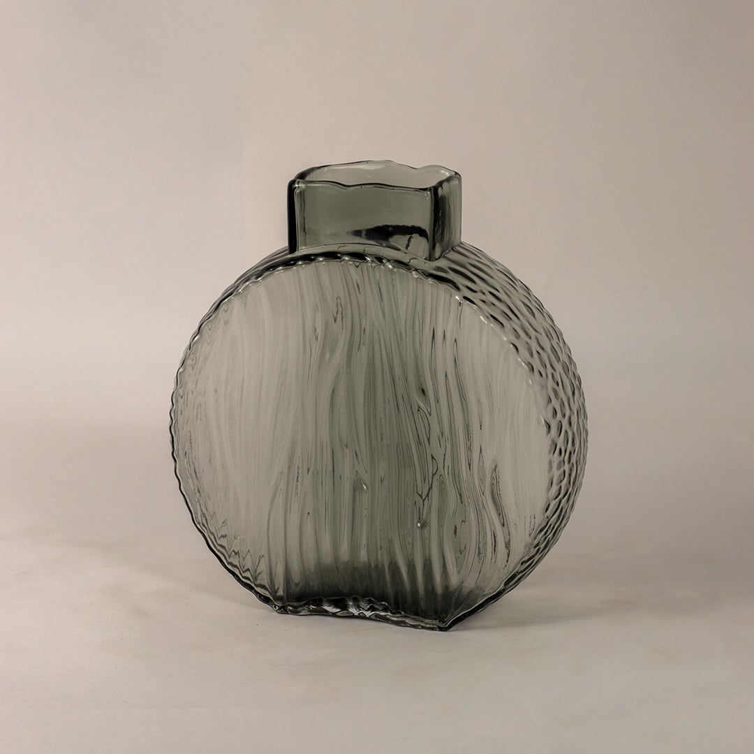 Side angle of round smoky gray glass vase showing its curved form  ribbed texture  and smooth reflective surface.