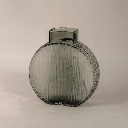 Side angle of round smoky gray glass vase showing its curved form  ribbed texture  and smooth reflective surface.