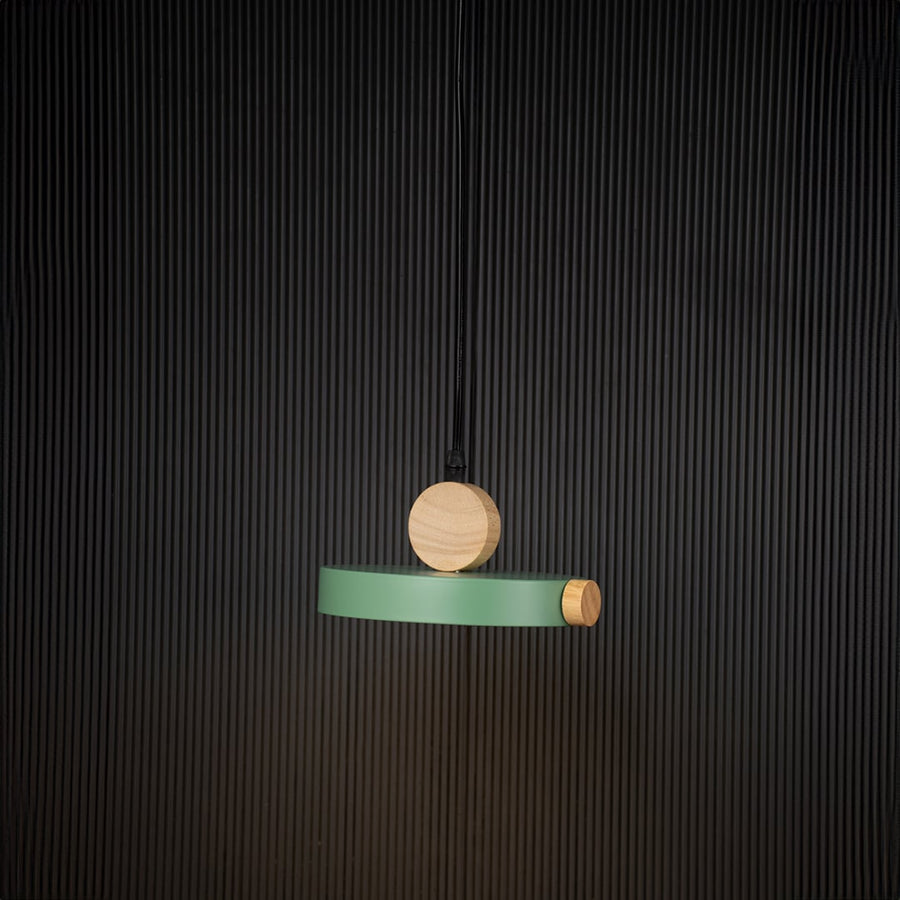 Green wood and metal pendant light glowing on black background with circular design for modern minimalist decor.