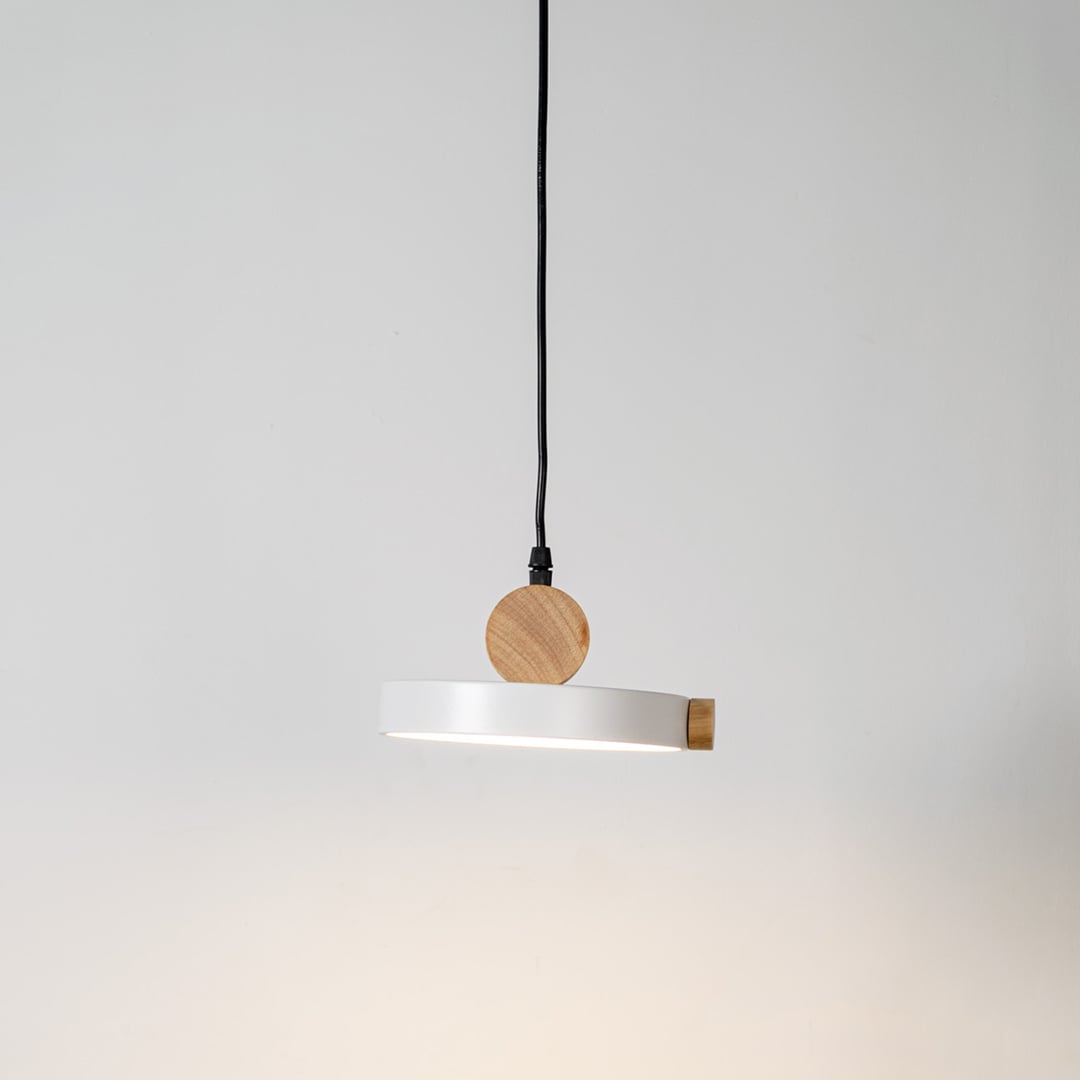 Pendant light glowing on white background with round flat metal shade and natural wood accents for modern interiors.