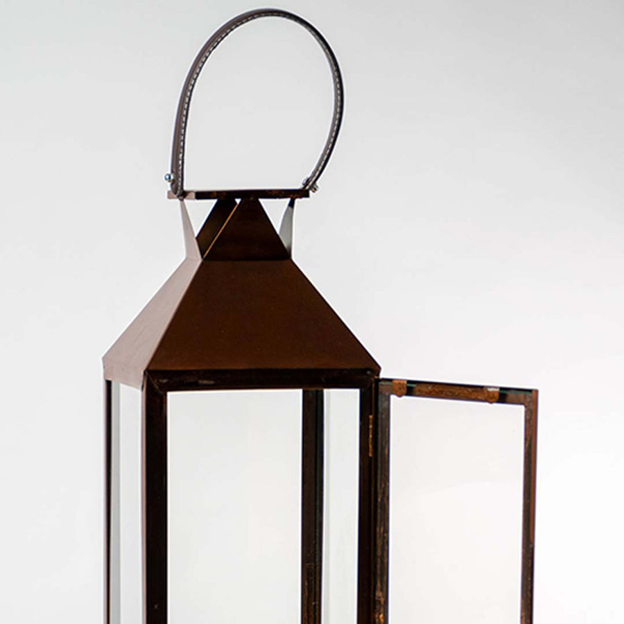 Closeup of copper metal lantern with glass panels and curved handle for luxury decor styling use.