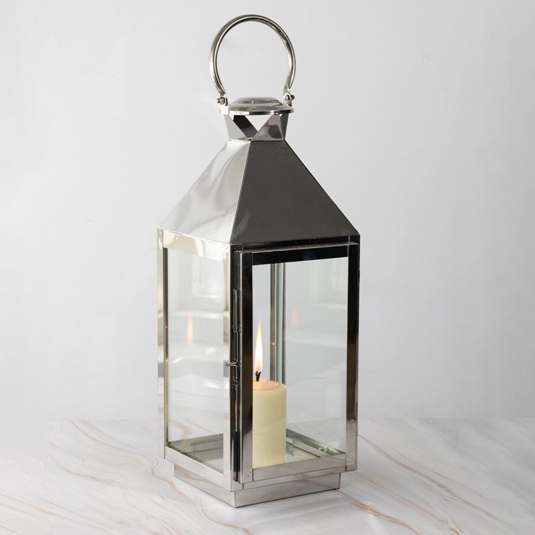 Large silver lantern with candle lit glowing softly against black background for stylish home lighting.