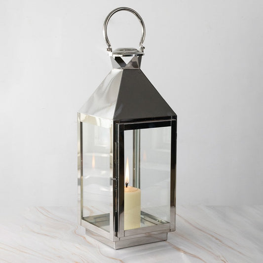 Large silver lantern with candle lit glowing softly against black background for stylish home lighting.