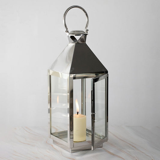 Stainless steel lantern with lit candle and glass panels displayed on white background for modern decor.