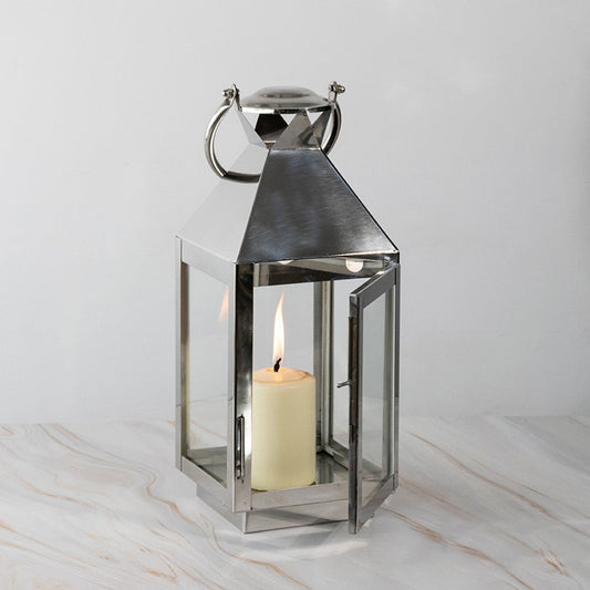 Tall stainless steel lantern with glass panels and candle lit displayed on white background for decor.
