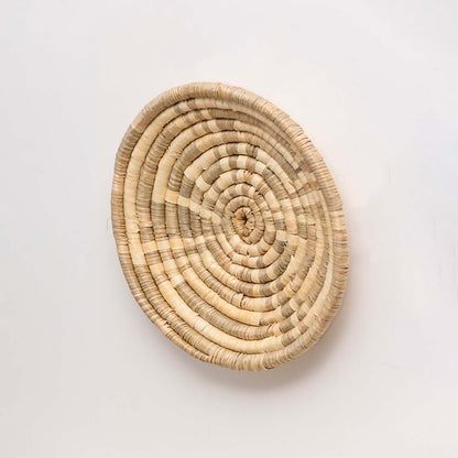 Side profile of the natural handwoven wall basket showing its shallow depth and circular handmade construction for wall mounting.