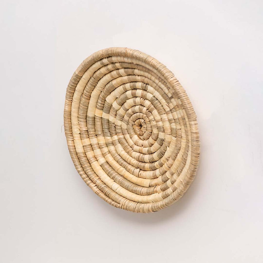 Side profile of the natural handwoven wall basket showing its shallow depth and circular handmade construction for wall mounting.